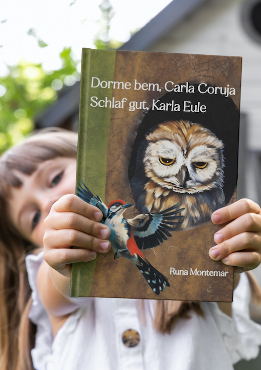 Ein Mädchen hält das Buch "Dorme Bem Carla Coruja, Schlaf gut, Karla Eule" in die Kamera.